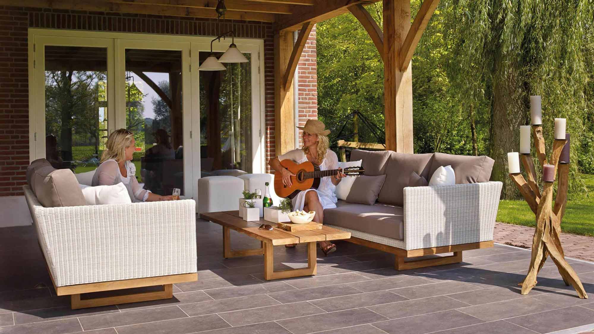 Two people sitting on a patio, one playing guitar, surrounded by outdoor furniture.