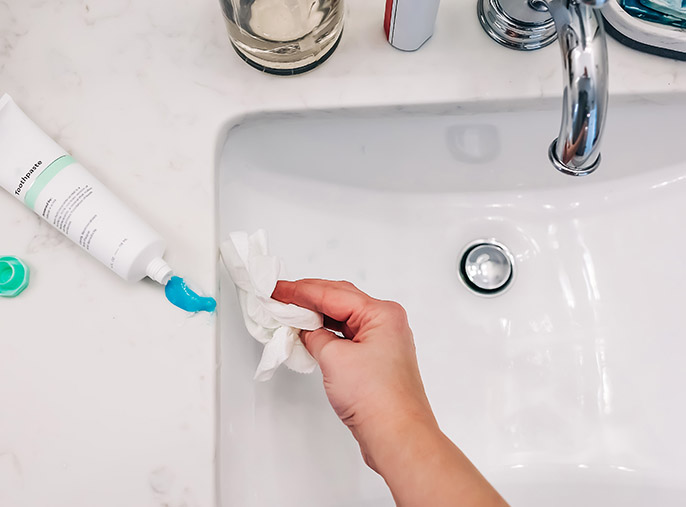 A hand cleaning a bathroom sink with a paper towel